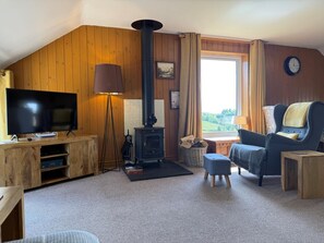 Ein gemütliches Wohnzimmer mit Fernseher, Kamin, einer Couch und einem Fenster mit Blick.