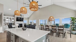 Cocina amplia con isla central, comedor con sillas y ventanas grandes que ofrecen una vista.