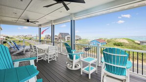 Una terraza techada con sillas y una mesa, con vista a una playa y casas.