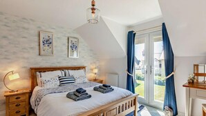 Un dormitorio con cama de madera, una mesita de noche, lámpara, luz de techo, ventana con cortinas y vistas al exterior.