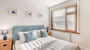 Ein Schlafzimmer mit Bett, Nachttischen, einem Fenster mit Jalousien und an der Wand befestigten Bilderrahmen.