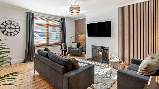 Ein modernes Wohnzimmer mit Sofa, Sessel, Kamin, Fernseher und einer Wanduhr.