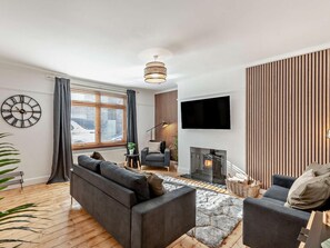 A modern living room with a sofa, armchair, fireplace, TV, and a clock on the wall. - 2 Bed in Seahouses (oc-cn006) (Seahouses)