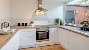 Eine moderne Küche mit weißen Schränken, einer Edelstahl-Dunstabzugshaube, einem eingebauten Backofen und einem Fenster mit Blick nach draußen.