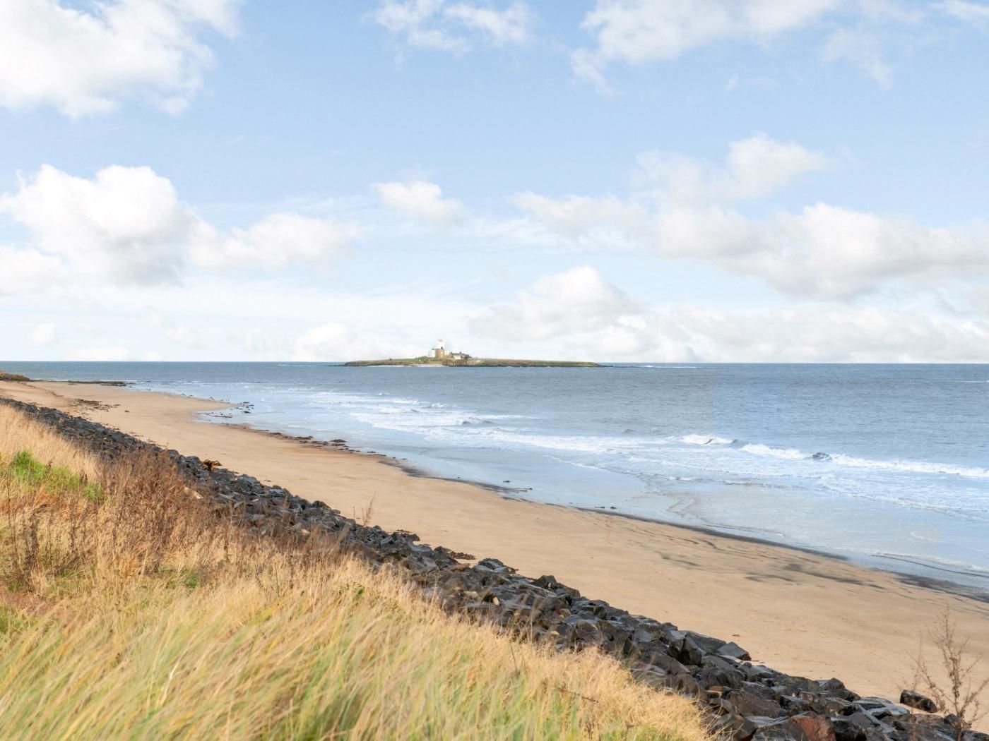 Een kuststrand met een rotsachtige kustlijn, een zandstrand en een eiland in de verte met een vuurtoren.