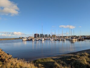 A marina with multiple boats docked, a pier, and buildings in the background. - 3 Bed in Morpeth (oc-cn027) (Low Hauxley)