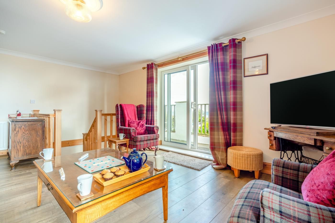 A living room with a wooden coffee table, a sofa, a television, and a balcony with curtains.