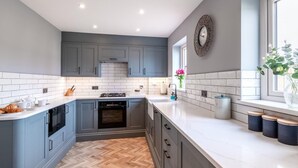 A modern kitchen with grey cabinets, white countertops, a herringbone floor, and a window with a view. - 2 Bed in Beadnell (oc-cn005) (Beadnell)