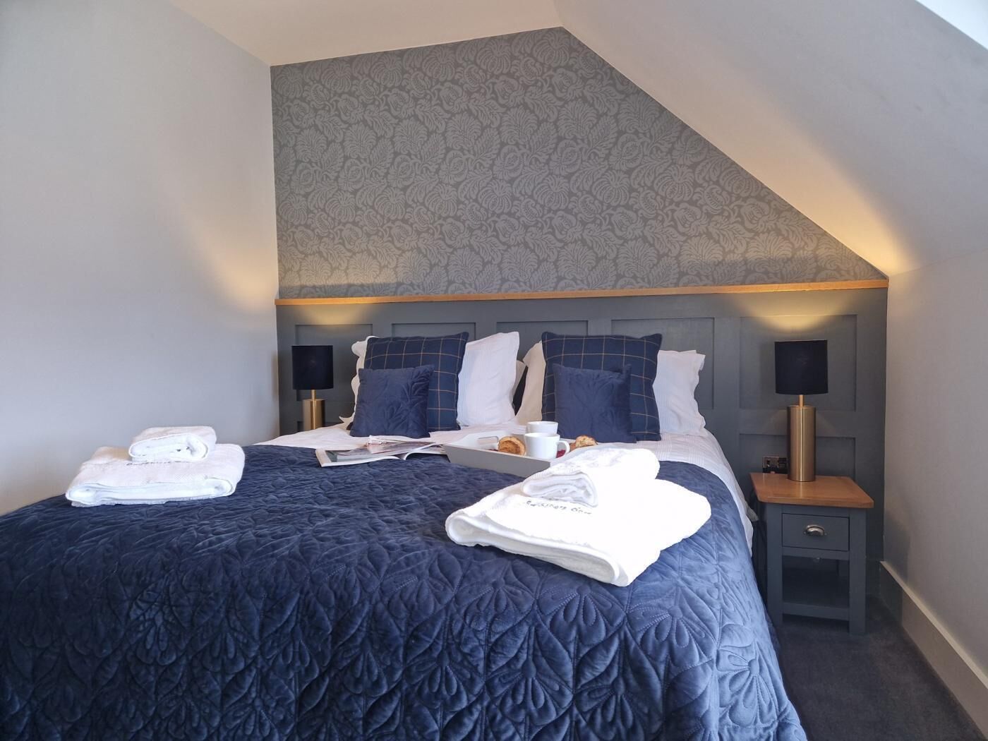 Ein Hotelzimmer mit einem großen Bett, zwei Nachttischen, einer gemusterten Decke und einer modernen Lampe.