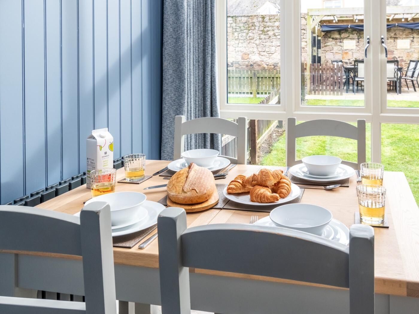 Une table de petit-déjeuner dressée avec des croissants, une miche de pain, un verre de jus de fruits et une bouteille de lait.