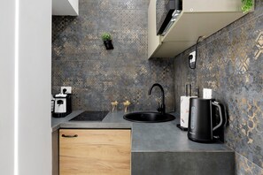 Eine moderne Küche mit einem schwarzen Spülbecken, einer Kaffeemaschine und einem kleinen Topfpflanzen an der Wand.