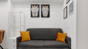 Una sala moderna con un sofá gris, dos cojines color mostaza, una mesita blanca y dos cuadros enmarcados en la pared.