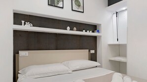 Una cama con sábanas blancas, un cabecero y una estantería con adornos.