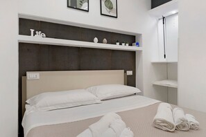 Ein Bett mit weißer Bettwäsche, einem Kopfteil und einem darüberliegenden Regal mit dekorativen Gegenständen.