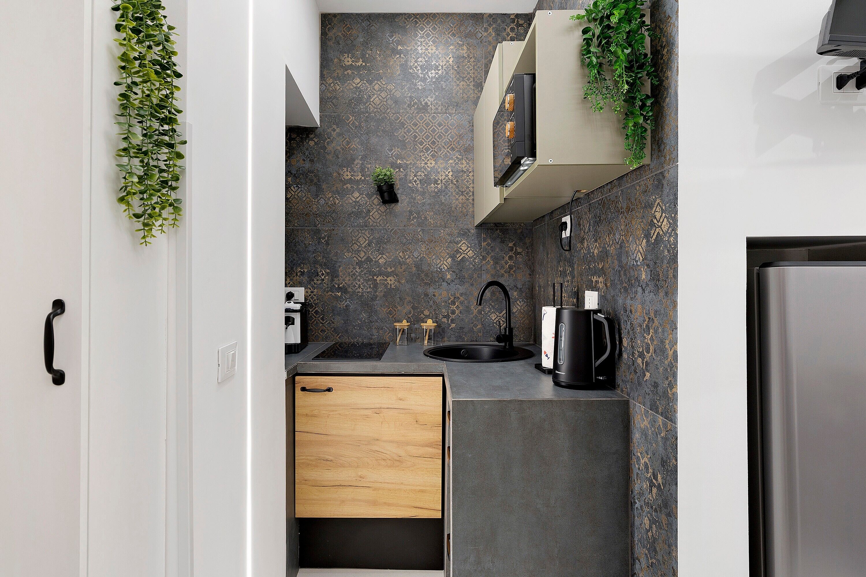 A compact kitchen with a wooden drawer, a black kettle, and a small potted plant on the wall.