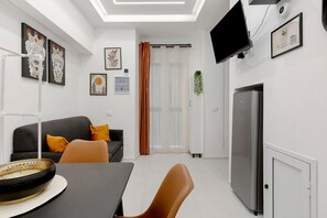 Un saló modern amb un sofà, una taula de dinar i una televisió plana penjada a la paret.