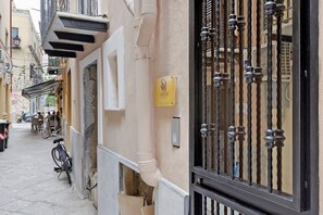 Eine schmale Straße mit Häusern an beiden Seiten, ein Fahrrad am Gehweg und ein schwarzes Tor mit einem Schild.