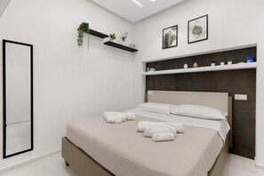 Ein modernes Schlafzimmer mit einem Bett, weißen Wänden, einer eingebauten Regalanlage mit Pflanzen und einer Tür.