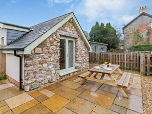 Une charmante maison en pierre dotée d’une terrasse carrelée et d’une table en bois, dressée pour le repas.