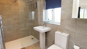 Un baño con cabina de ducha de vidrio, lavamanos pedestal, inodoro y ventana con vistas.