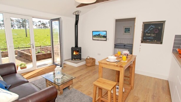 Un salón acogedor con chimenea, comedor y vistas a un paisaje verde a través de amplios ventanales.