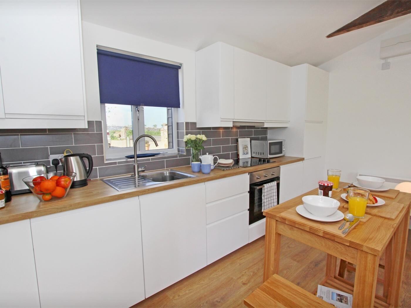 A modern kitchen with white cabinets, a sink, a microwave, and a dining area with a table set for breakfast.