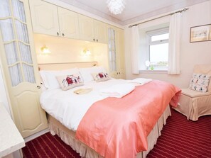A bedroom with a bed, a window with curtains, a chair, and a wall-mounted light fixture. - 3 Bed in Low Newton - By- The -sea (oc-cn009) (Newton-by-the-Sea)