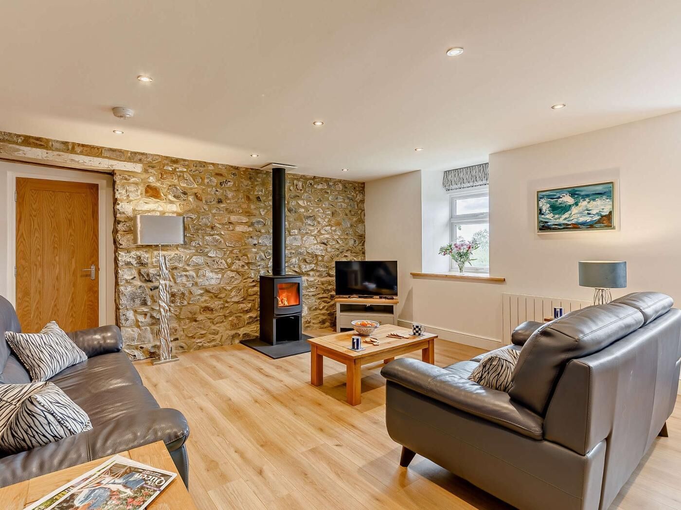 Ein Wohnzimmer mit Steinwand, Kamin, Fernseher, Ledersofas und einem Couchtisch aus Holz.