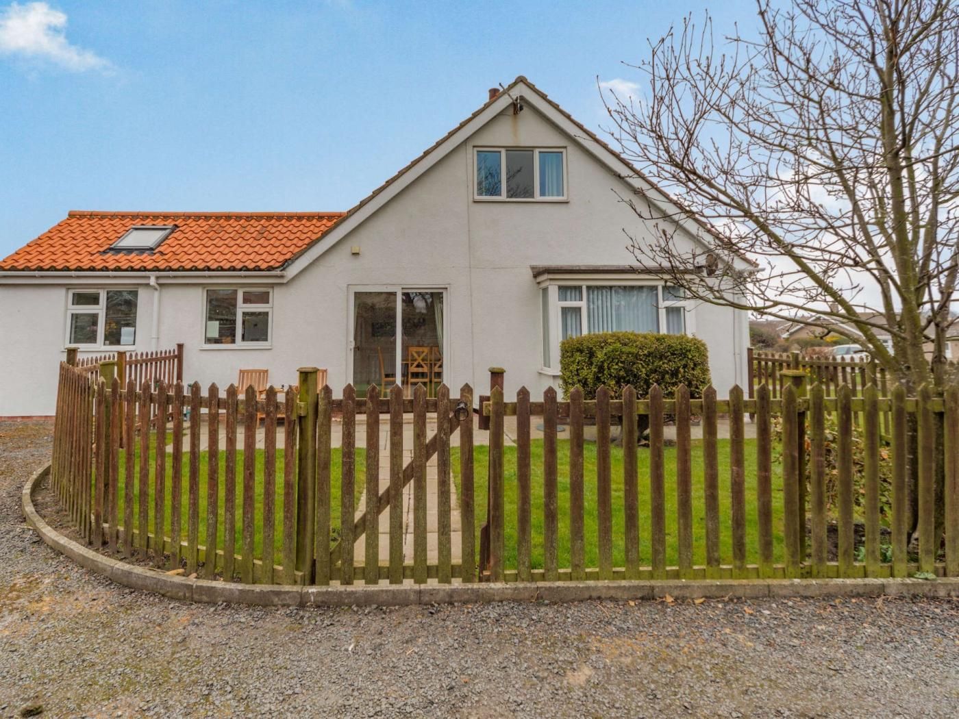 A two-story house with a red-tiled roof, a wooden fence, and a gravel driveway.