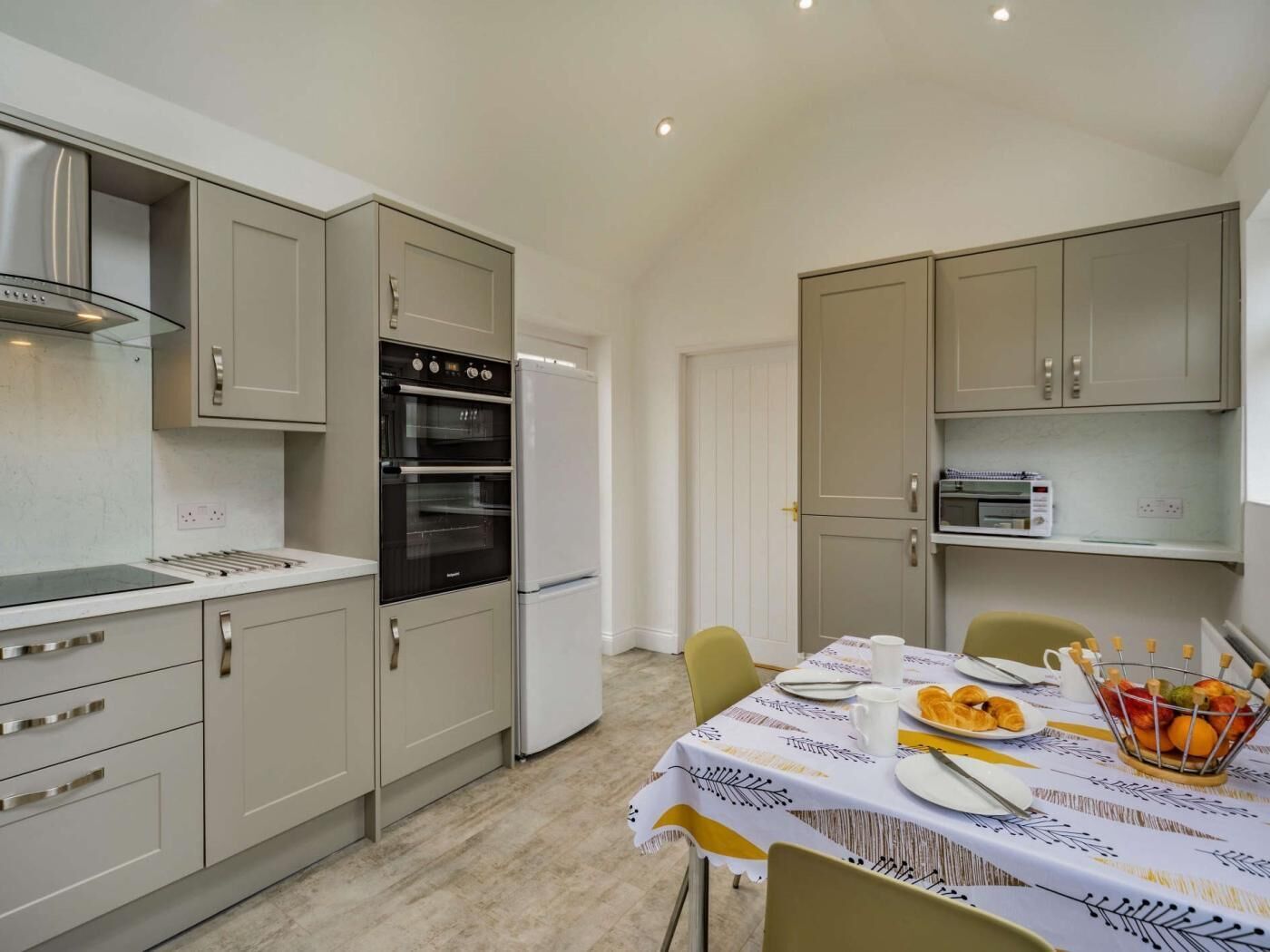 A compact kitchen with a built-in oven, a refrigerator, and a dining area with a table set for breakfast.