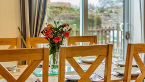 Una mesa de comedor con sillas, un florero con flores y vistas a través de un ventanal.