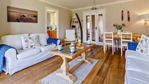 A living room with a sofa, coffee table, dining table, chairs, and a kitchen in the background. - 2 Bed in Chathill (oc-cn028) (Beadnell)