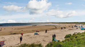 A beach with people, a boat, and a clear sky. - 2 Bed in Chathill (oc-cn028) (Beadnell)