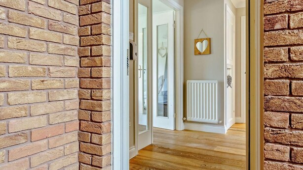 A hallway with brick walls, a wooden floor, a white radiator, and a ceiling light fixture. - 2 Bed in Chathill (oc-cn028) (Beadnell)