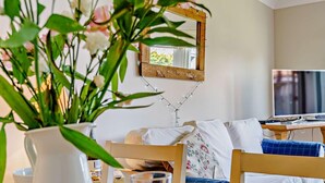 A dining area with a wooden table, chairs, a white vase with flowers, a glass of orange juice, and a television in the background. - 2 Bed in Chathill (oc-cn028) (Beadnell)