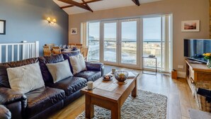 Ein Wohnzimmer mit Ledersofa, Holztisch und einem großen Fenster mit Meerblick.