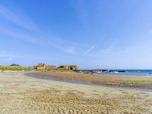 A beach with a sandy shore, a large building with a red roof, and several boats in the water. - 3 Bed in Beadnell (oc-cn042) (Beadnell)