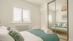 Un dormitorio con cama, un radiador, una ventana con persianas, un espejo y una lámpara en el techo.