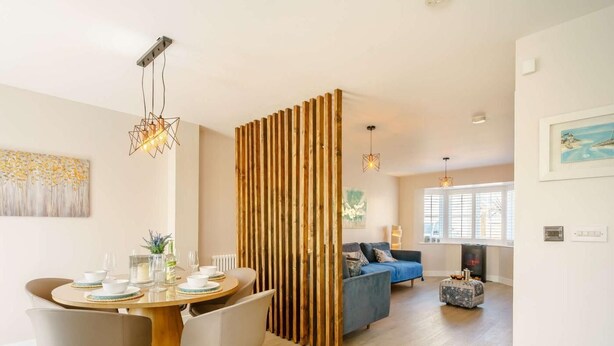 Un espacio habitable moderno con zona de comedor, un sofá azul y un panel de madera decorativo.