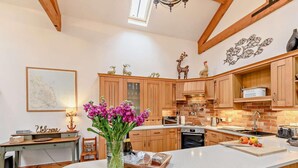 A kitchen with wooden cabinets, a central island, a chandelier, and a decorative wall piece. - 3 Bed in Beadnell (oc-cn037) (Beadnell)
