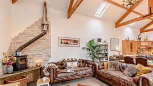 A cozy living room with a fireplace, leather sofas, a cowhide rug, and a staircase. - 3 Bed in Beadnell (oc-cn037) (Beadnell)