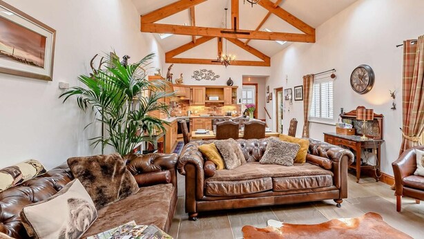 A spacious living room with a high ceiling, wooden beams, a chandelier, a dining area, and a kitchen in the background. - 3 Bed in Beadnell (oc-cn037) (Beadnell)