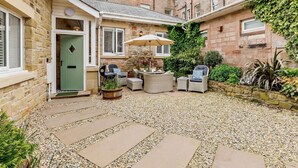 A courtyard with stone flooring, outdoor seating, and a green door. - 3 Bed in Beadnell (oc-cn037) (Beadnell)
