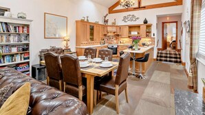 A spacious living area with a dining table, leather sofa, and a kitchen with wooden beams and a skylight. - 3 Bed in Beadnell (oc-cn037) (Beadnell)