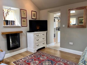 A living room with a fireplace, a television, a patterned rug, and a kitchen visible through an open doorway. - 1 Bed in Riding Mill (oc-cn063) (Corbridge)