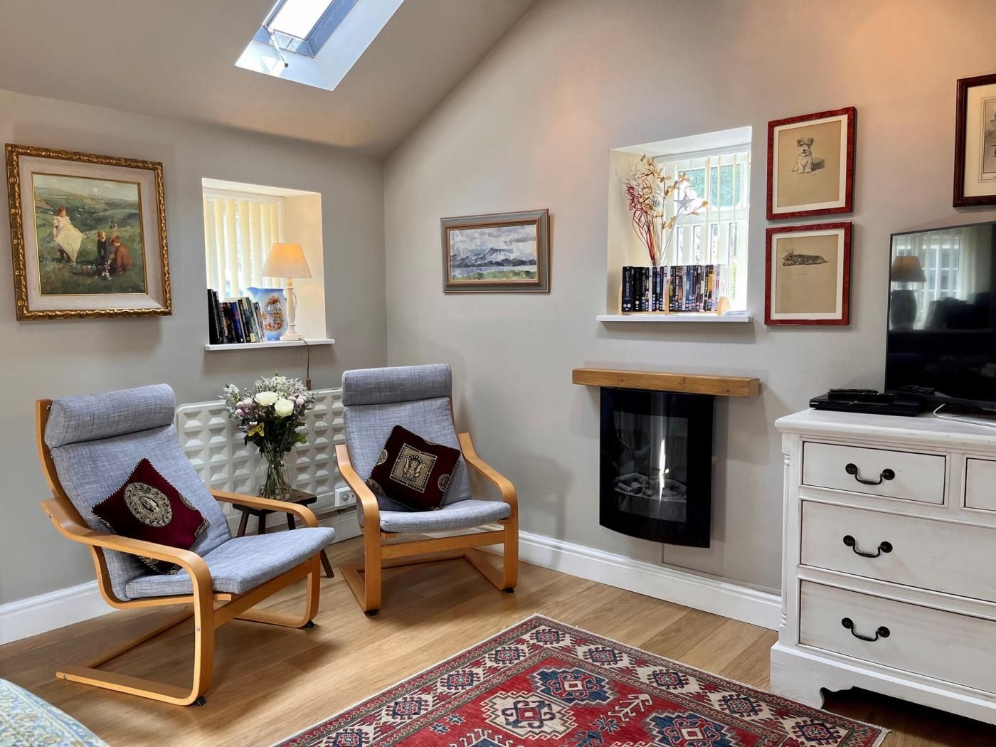 A living room with two armchairs, a fireplace, a TV, and a bookshelf with books and framed pictures.