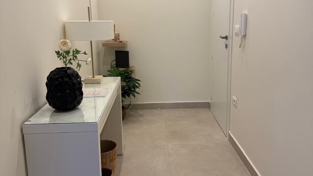 A narrow hallway with a white door, a small table with a lamp, and a potted plant. - The Bacchae - Urban Apartment (Siracusa)