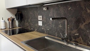 A modern kitchen with a black marble backsplash, stainless steel sink, and wooden countertop. - The Bacchae - Urban Apartment (Siracusa)