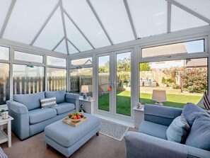 A conservatory with a sofa, ottoman, and a table with fruit. - 3 Bed in Seahouses (oc-cn064) (Seahouses)