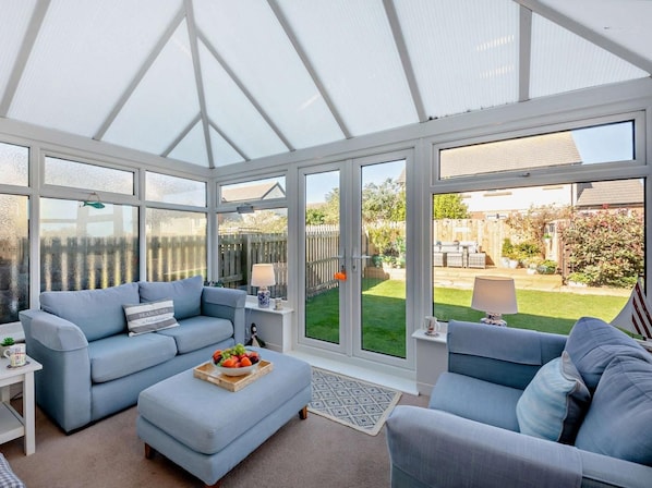 A conservatory with a sofa, ottoman, and a table with fruit. - 3 Bed in Seahouses (oc-cn064) (Seahouses)